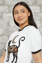 A woman wearing a white ringer t-shirt with black trim and a colorful floral cat graphic, photographed against a solid white background.