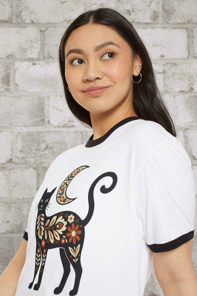 A woman wearing a white ringer t-shirt with black trim and a colorful floral cat graphic, photographed against a solid white background.