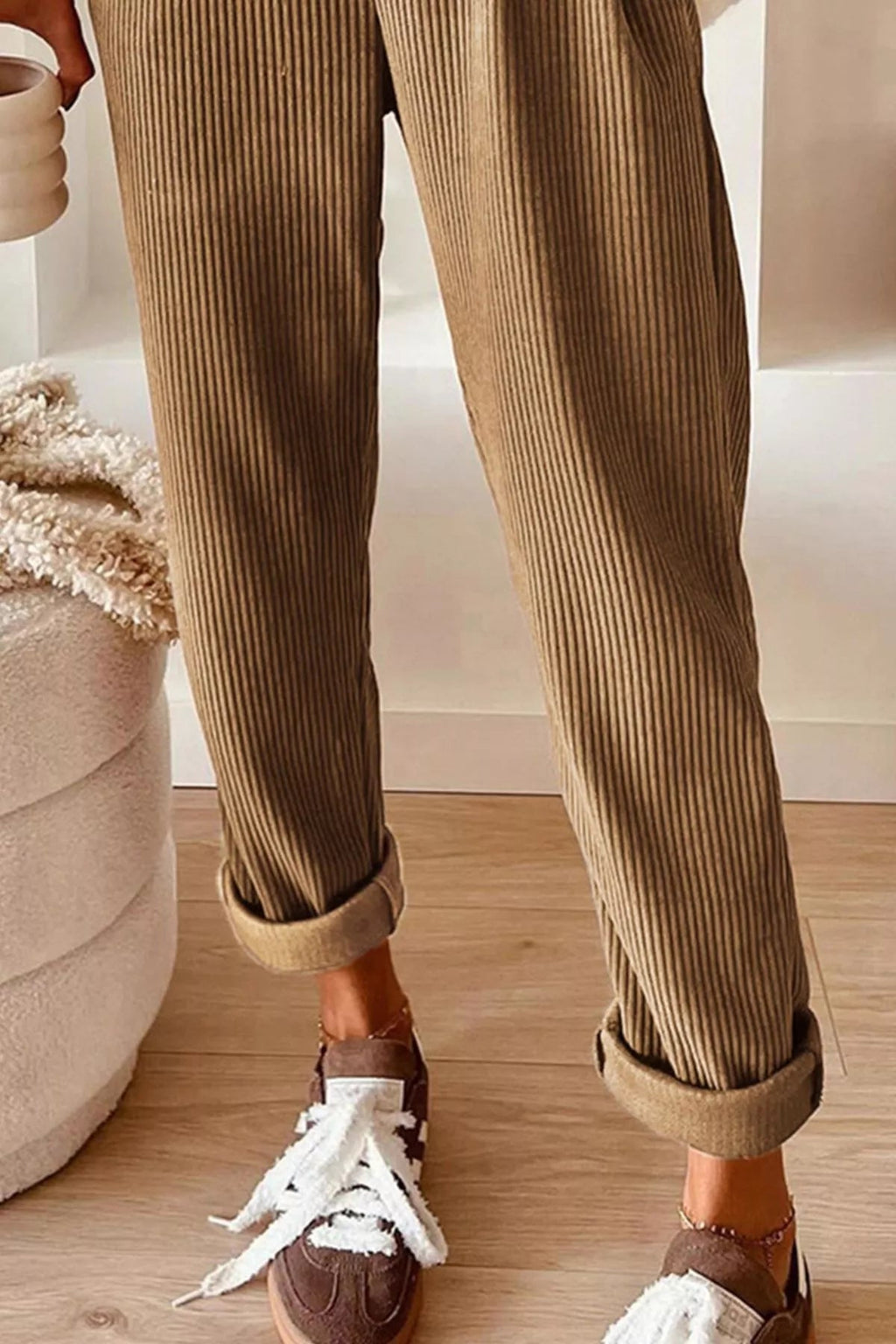 Person wearing brown corduroy pants and brown shoes with white laces on a wooden floor.
