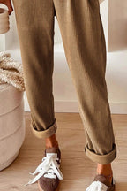 Person wearing brown corduroy pants and brown shoes with white laces on a wooden floor.