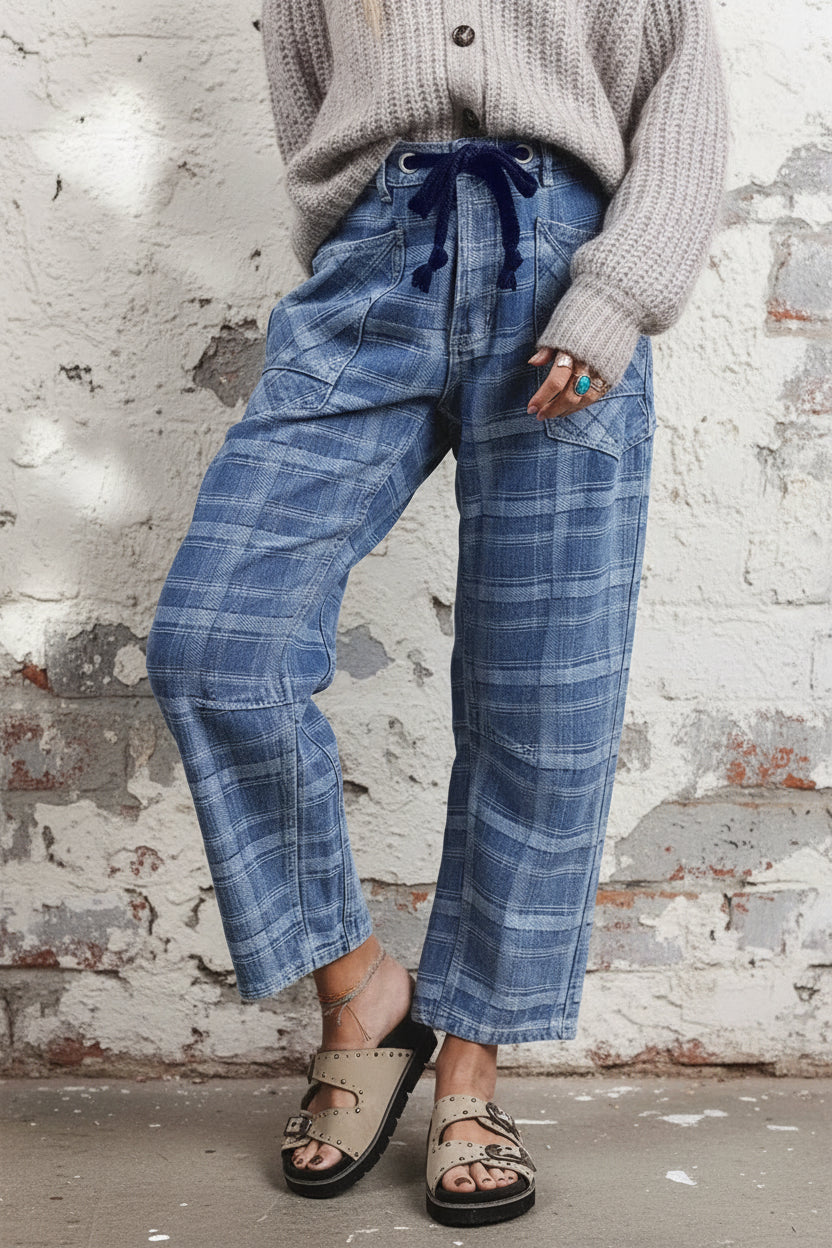 A person wearing blue plaid cropped pants with a dark blue drawstring waist, styled with a light gray knit sweater and beige sandals against a neutral indoor background.