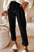 Person wearing black ribbed pants and a white sweater, holding a ceramic cup indoors.