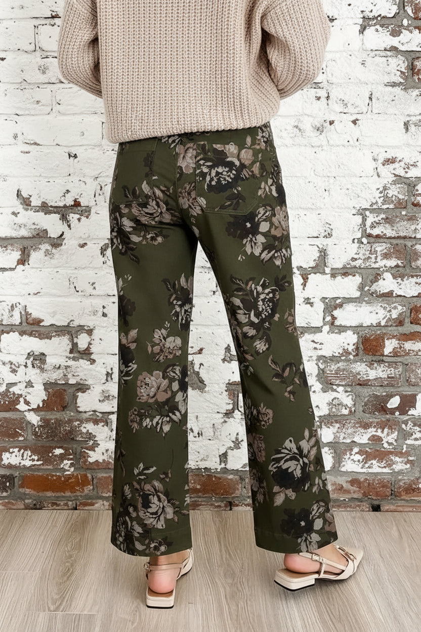 Green floral pants worn by a person on a light wooden floor.