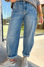 Person wearing blue jeans and white sneakers standing on a sidewalk.