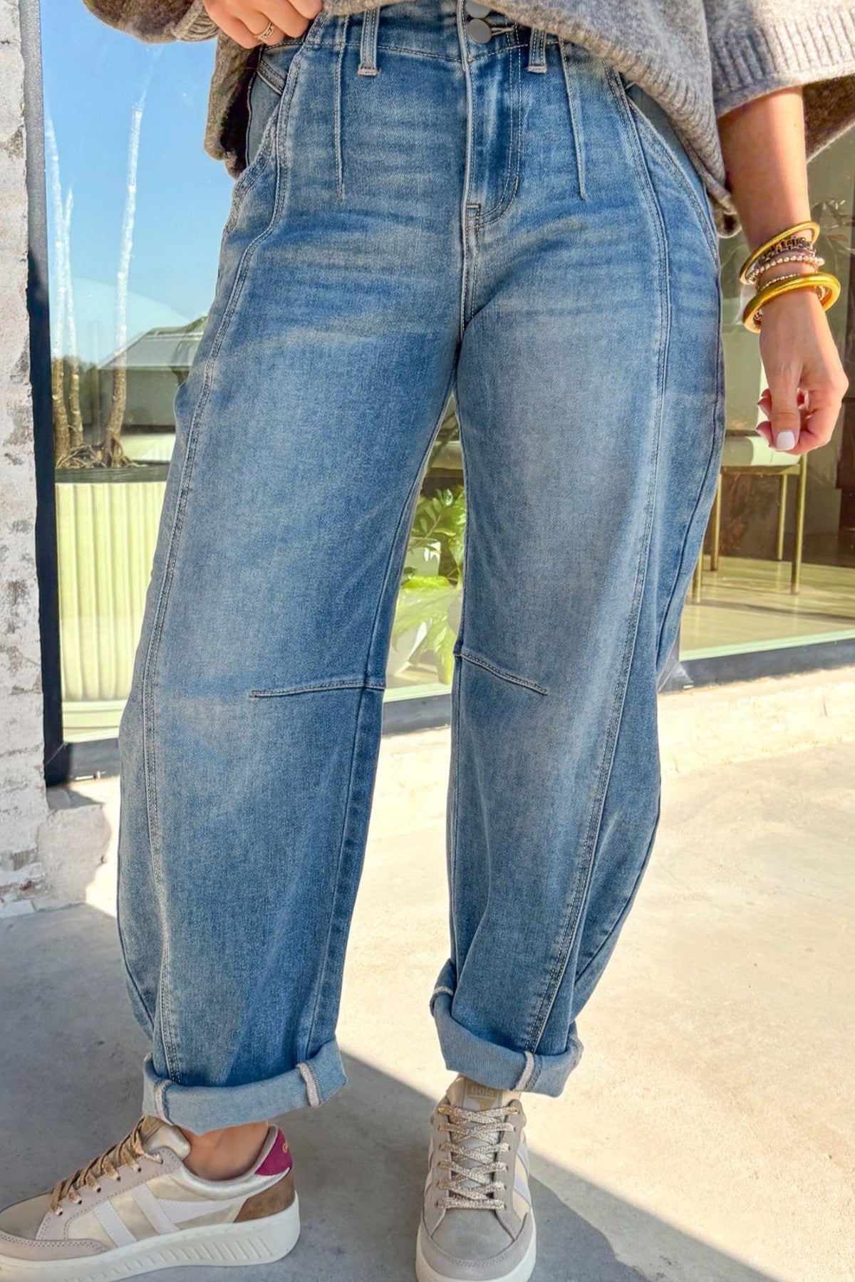 Person wearing blue jeans and white sneakers standing on a sidewalk.