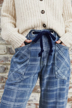 A close-up of a person wearing blue plaid wide-leg jeans with a dark navy drawstring waist and a chunky light gray knit cardigan.