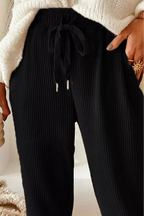Person wearing black ribbed pants with a white sweater and beige blanket in the background