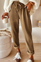 Person wearing brown ribbed pants with a white top and sneakers, holding a ceramic cup.