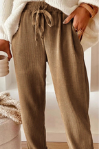 Person wearing brown ribbed pants holding a white mug indoors.