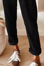 Person wearing black ribbed pants with white sneakers on a wooden floor.
