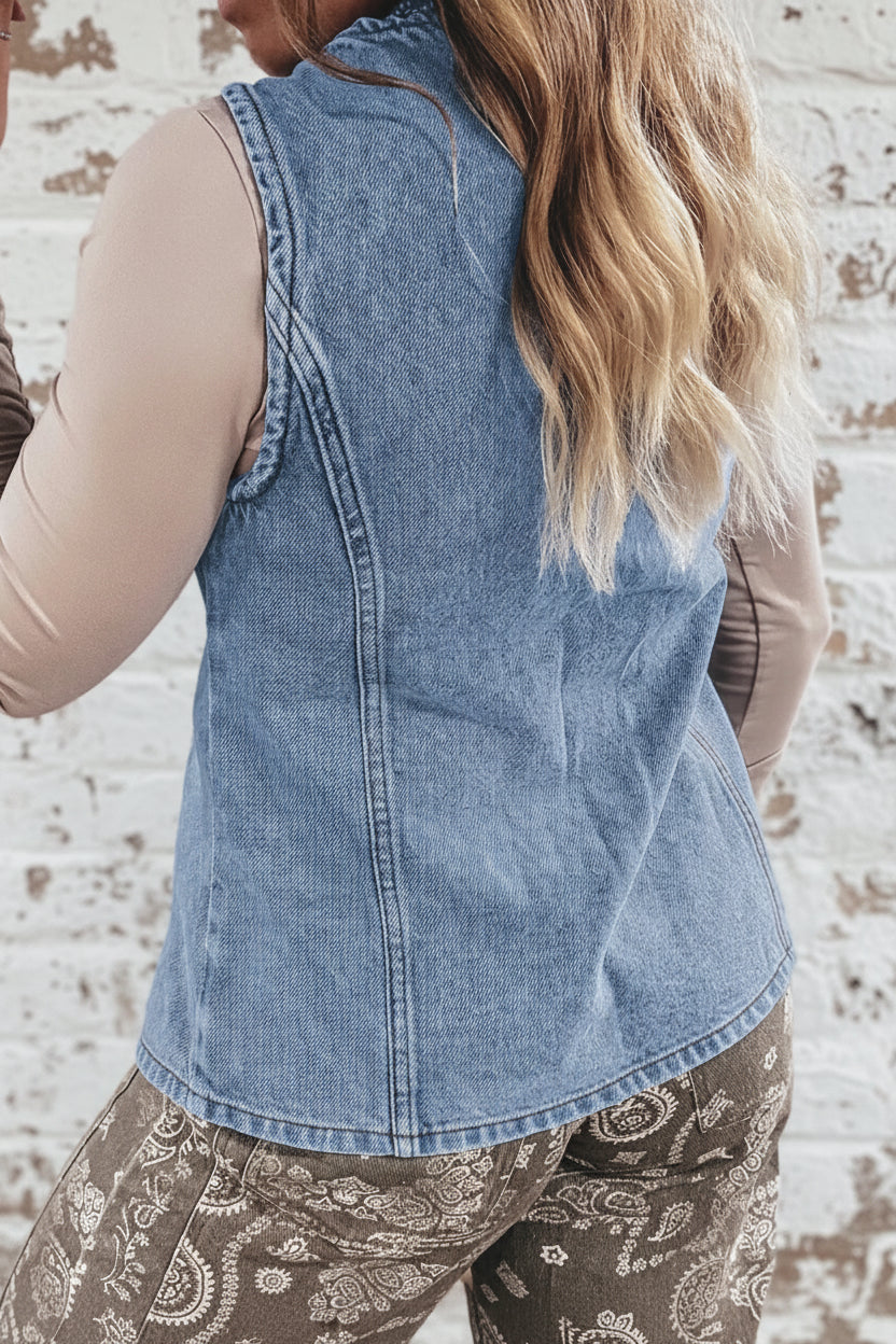 Person wearing a denim vest over a beige top with a blurred indoor background