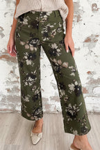 A person wearing olive green wide-leg cropped pants with a black and beige floral print, paired with a cream knit top and pointed flats, standing against a white wall and light wood floor.