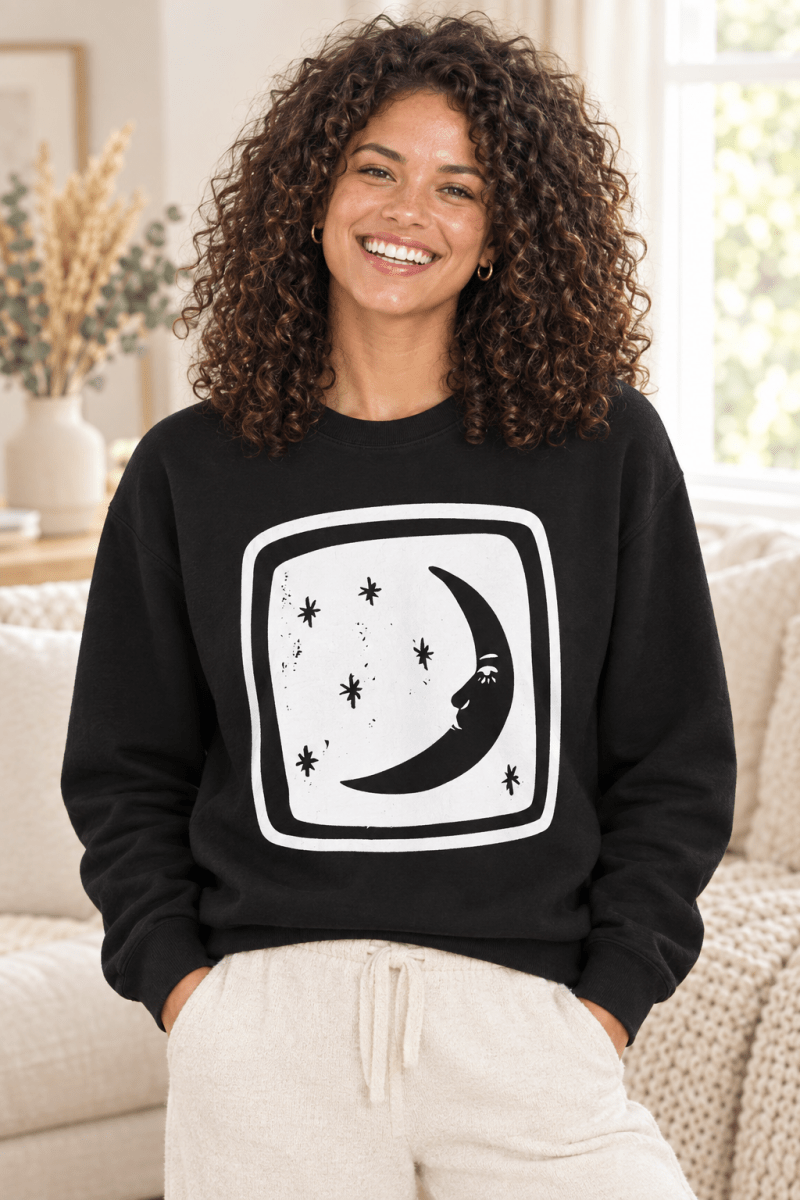 The Doodled Flower Boutique black crewneck sweatshirt featuring an original crescent moon and stars graphic, close up.