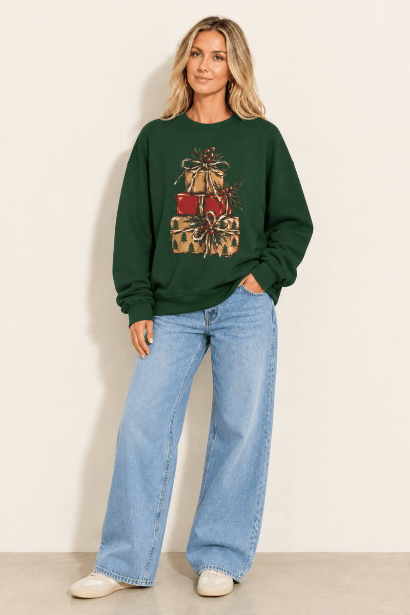 The Doodled Flower Boutique forest green crewneck sweatshirt featuring a stacked presents graphic with evergreen sprigs and red berries, worn by a model.