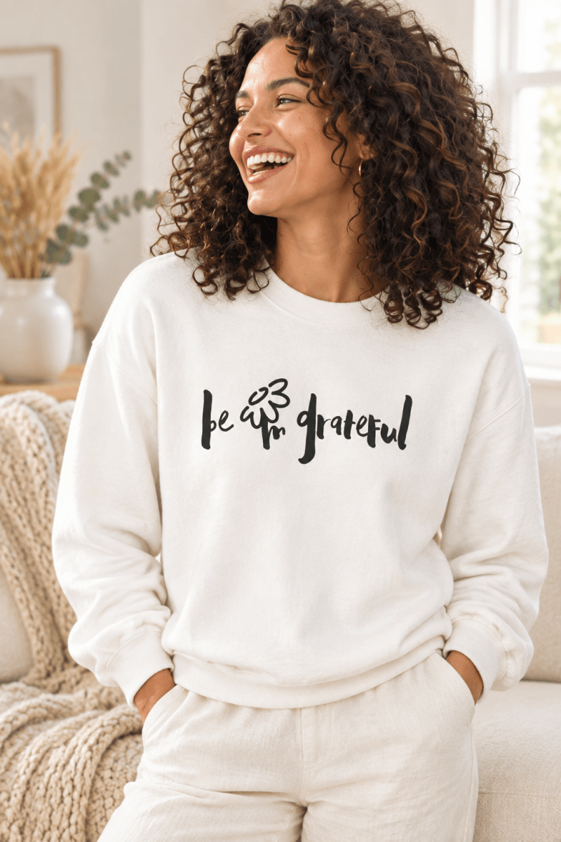 The Doodled Flower Boutique white crewneck sweatshirt featuring an original hand-lettered be grateful graphic with a doodled daisy, close up.
