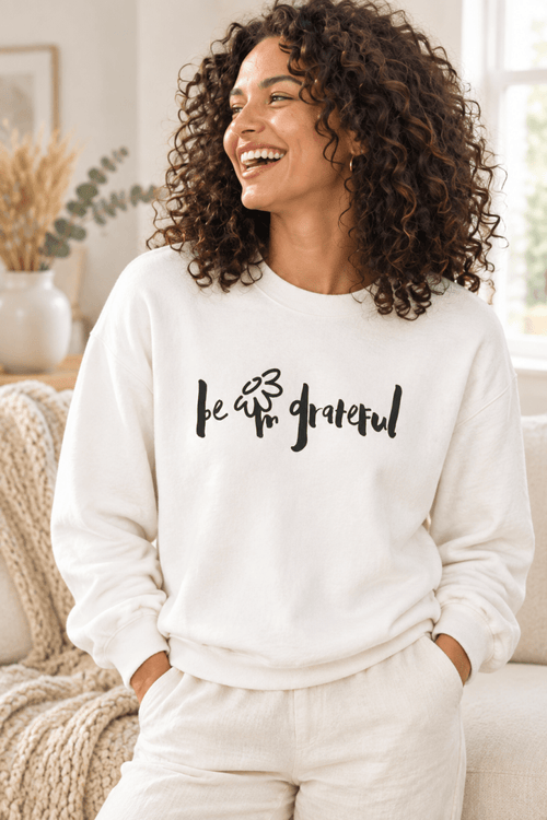 The Doodled Flower Boutique white crewneck sweatshirt featuring an original hand-lettered be grateful graphic with a doodled daisy, close up.