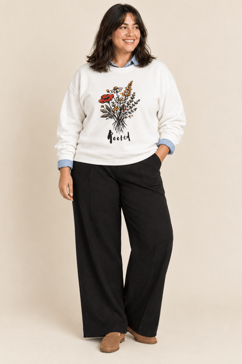 The Doodled Flower Boutique white rooted floral crewneck sweatshirt layered over a chambray button-down with black wide leg trousers and loafers.