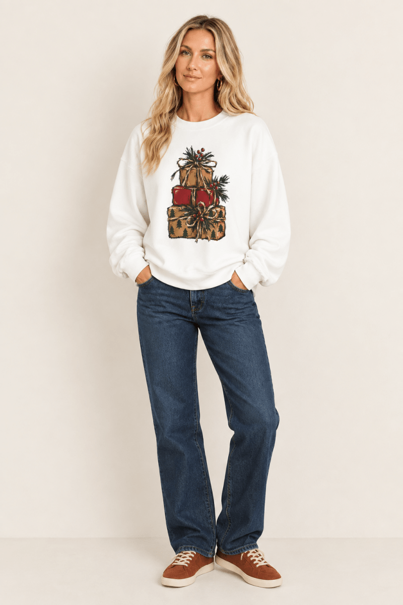 The Doodled Flower Boutique white crewneck sweatshirt featuring a stacked presents graphic with evergreen sprigs and red berries, worn by a model.