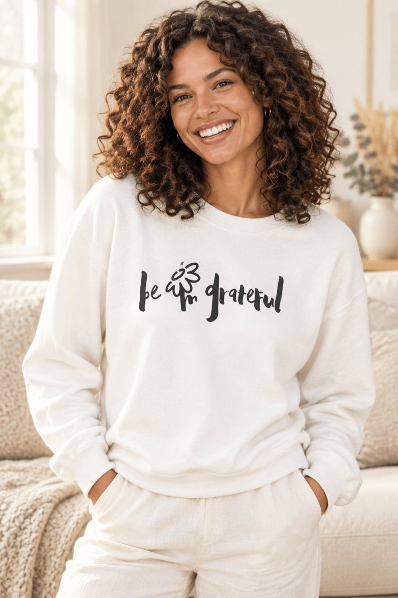 The Doodled Flower Boutique white crewneck sweatshirt featuring an original hand-lettered be grateful graphic with a doodled daisy, close up.