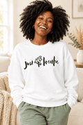 The Doodled Flower Boutique white crewneck sweatshirt featuring an original hand-lettered just breathe graphic with a doodled daisy, close up.