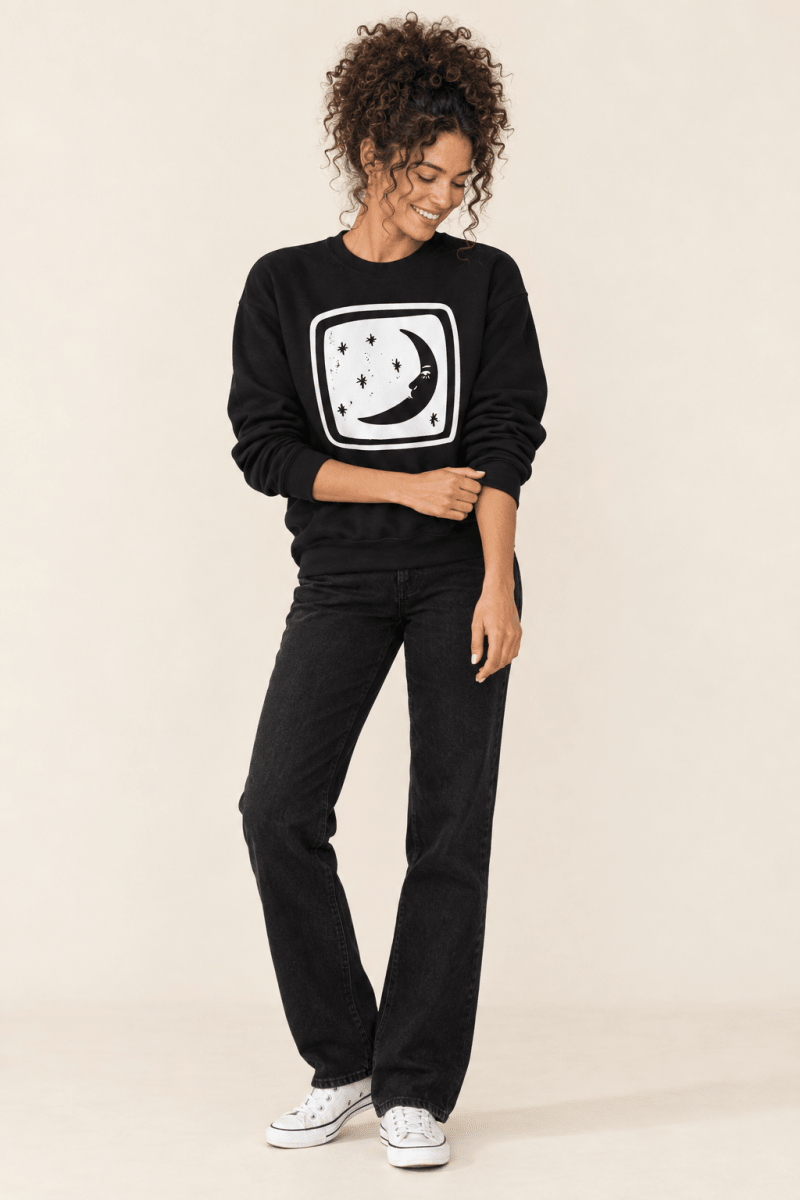 The Doodled Flower Boutique black crescent moon and stars crewneck sweatshirt styled with black straight jeans and white canvas sneakers.