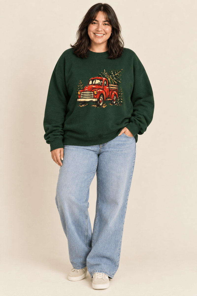 The Doodled Flower Boutique forest green crewneck sweatshirt featuring a textless vintage red Christmas truck carrying an evergreen tree graphic, worn by a model.