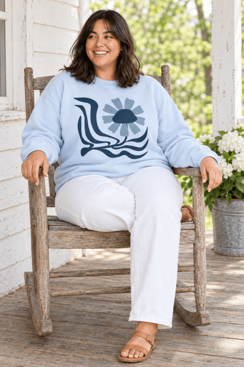 The Doodled Flower Boutique light blue retro floral wave crewneck sweatshirt styled with white jeans and sandals in a porch rocking chair.
