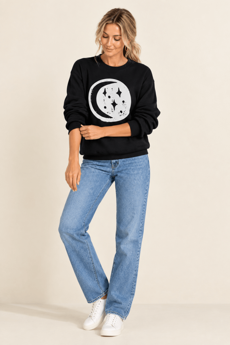 The Doodled Flower Boutique black moon and stars crewneck sweatshirt styled with straight leg jeans and white sneakers.