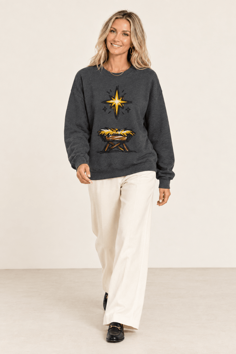 The Doodled Flower Boutique dark heather star of Bethlehem crewneck sweatshirt worn by a model with ivory wide leg trousers and black loafers.