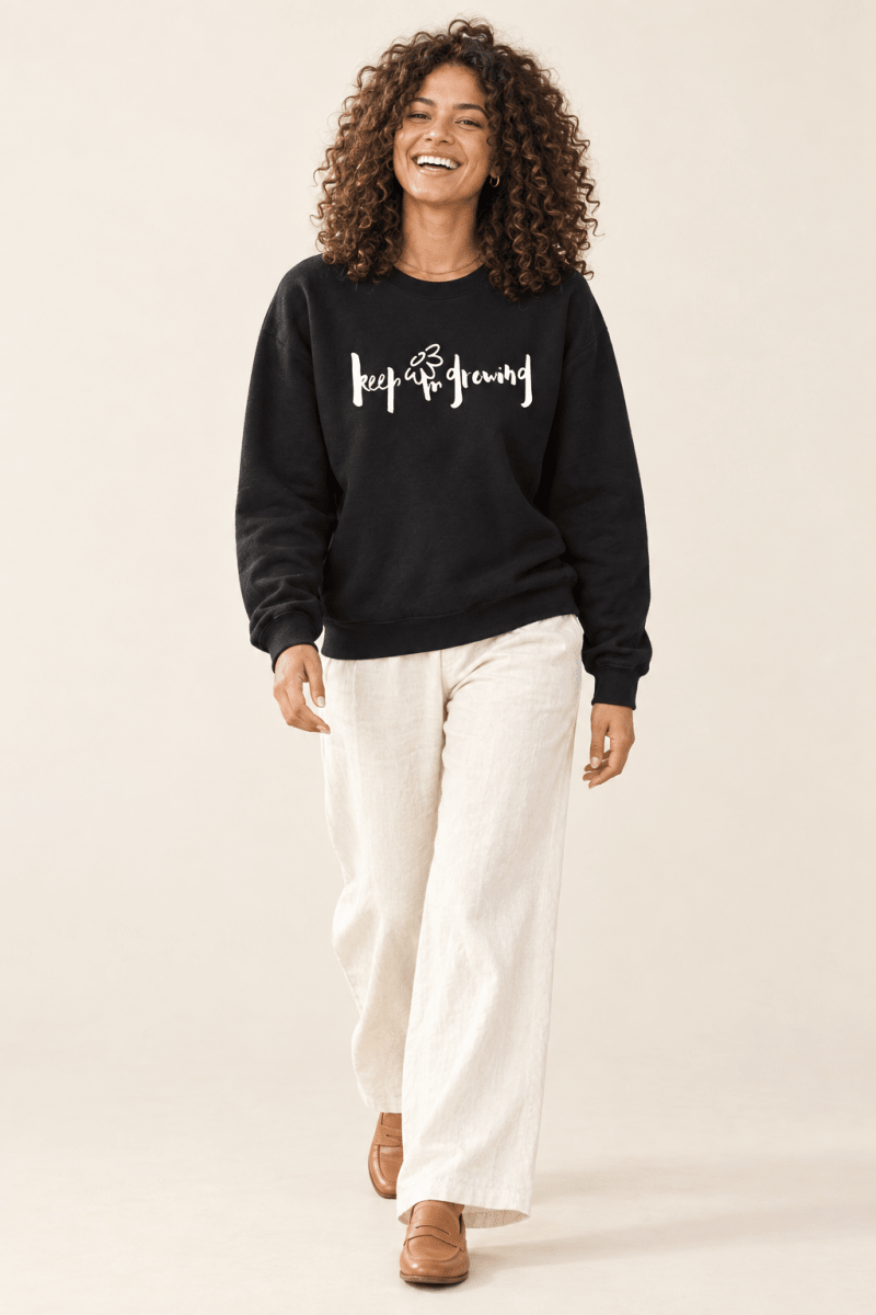 The Doodled Flower Boutique black keep growing crewneck sweatshirt worn by a model with ivory wide leg trousers and tan loafers.