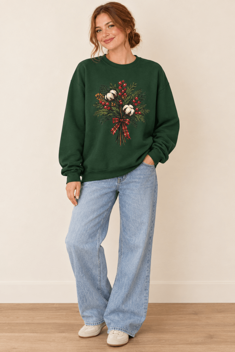 The Doodled Flower Boutique forest green crewneck sweatshirt featuring a cotton bouquet with red berries and a plaid bow graphic, worn by a model.