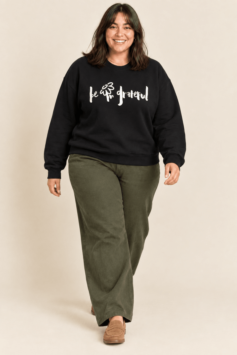 The Doodled Flower Boutique black be grateful crewneck sweatshirt worn by a model with olive wide leg trousers and suede loafers.