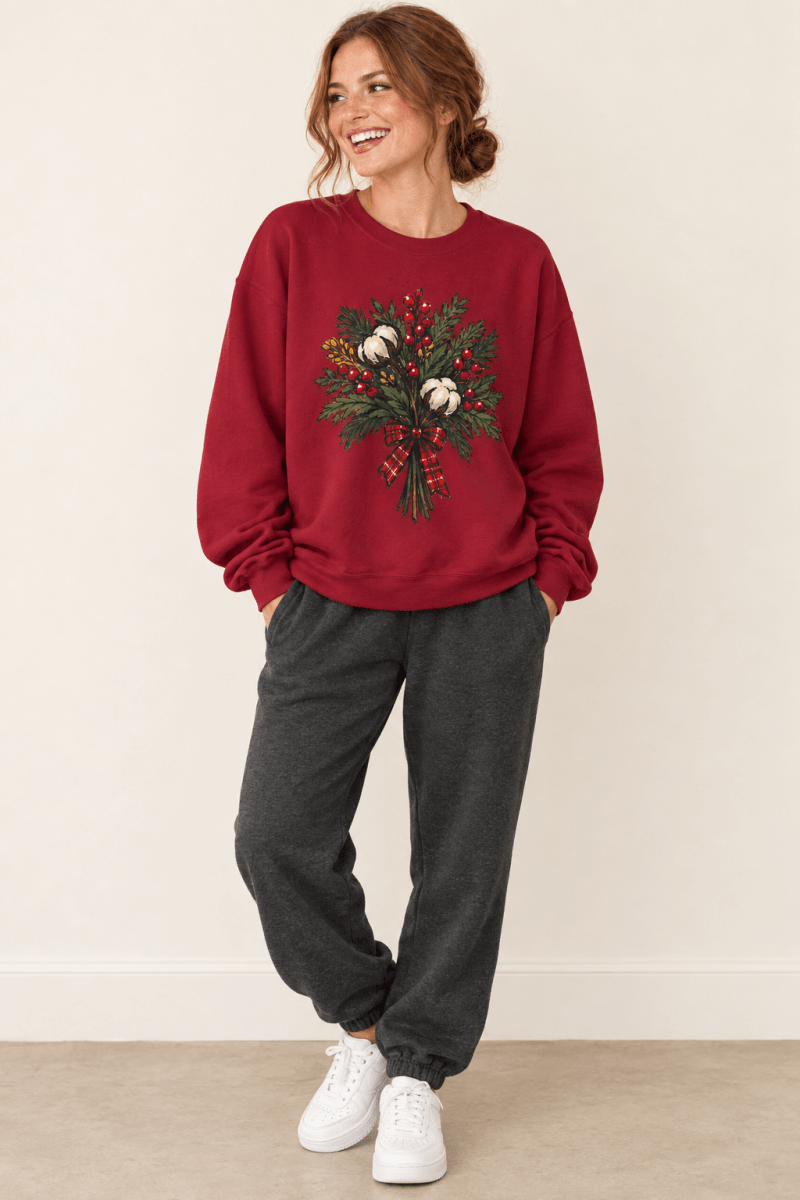 The Doodled Flower Boutique cardinal red crewneck sweatshirt featuring a cotton bouquet with red berries and a plaid bow graphic, worn by a model.