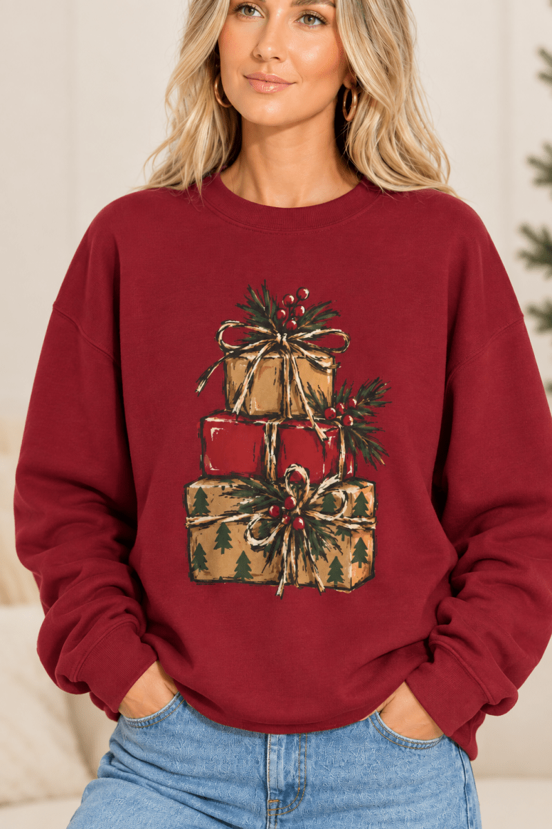 The Doodled Flower Boutique cardinal red crewneck sweatshirt featuring a stacked presents graphic with evergreen sprigs and red berries, close up.