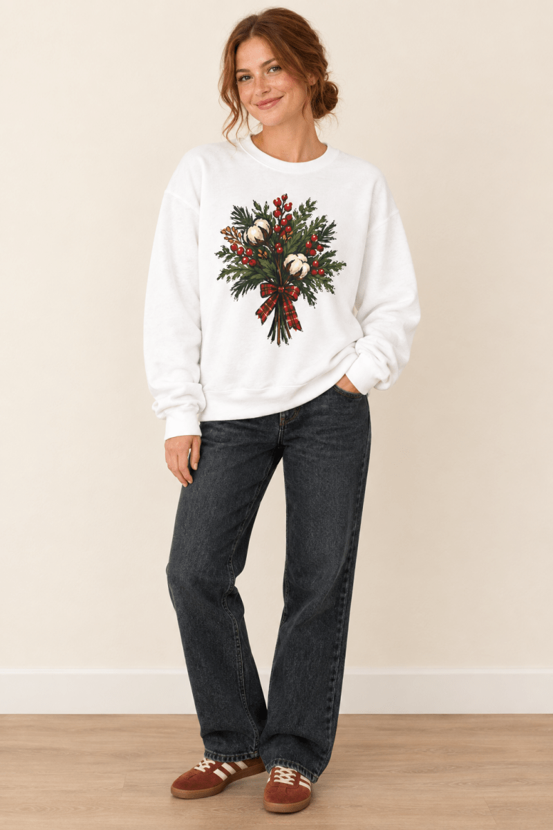 The Doodled Flower Boutique white crewneck sweatshirt featuring a cotton bouquet with red berries and a plaid bow graphic, worn by a model.