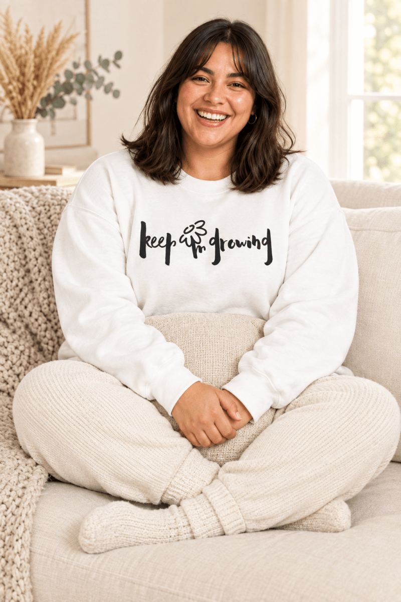 The Doodled Flower Boutique white keep growing crewneck sweatshirt styled with ivory knit joggers on a cozy cream sofa.