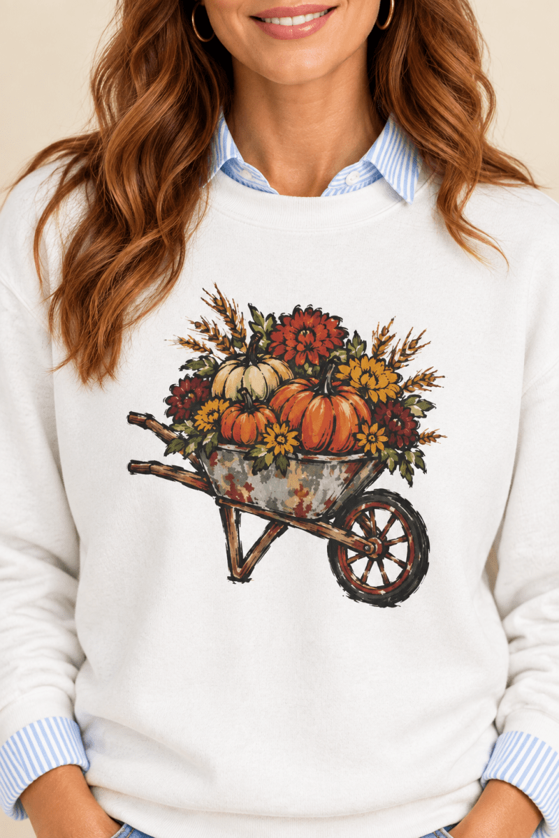 The Doodled Flower Boutique white crewneck sweatshirt featuring a rustic autumn wheelbarrow of pumpkins and mums graphic, close up