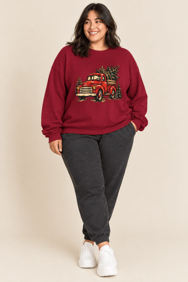 The Doodled Flower Boutique cardinal red crewneck sweatshirt featuring a textless vintage red Christmas truck carrying an evergreen tree graphic, worn by a model.