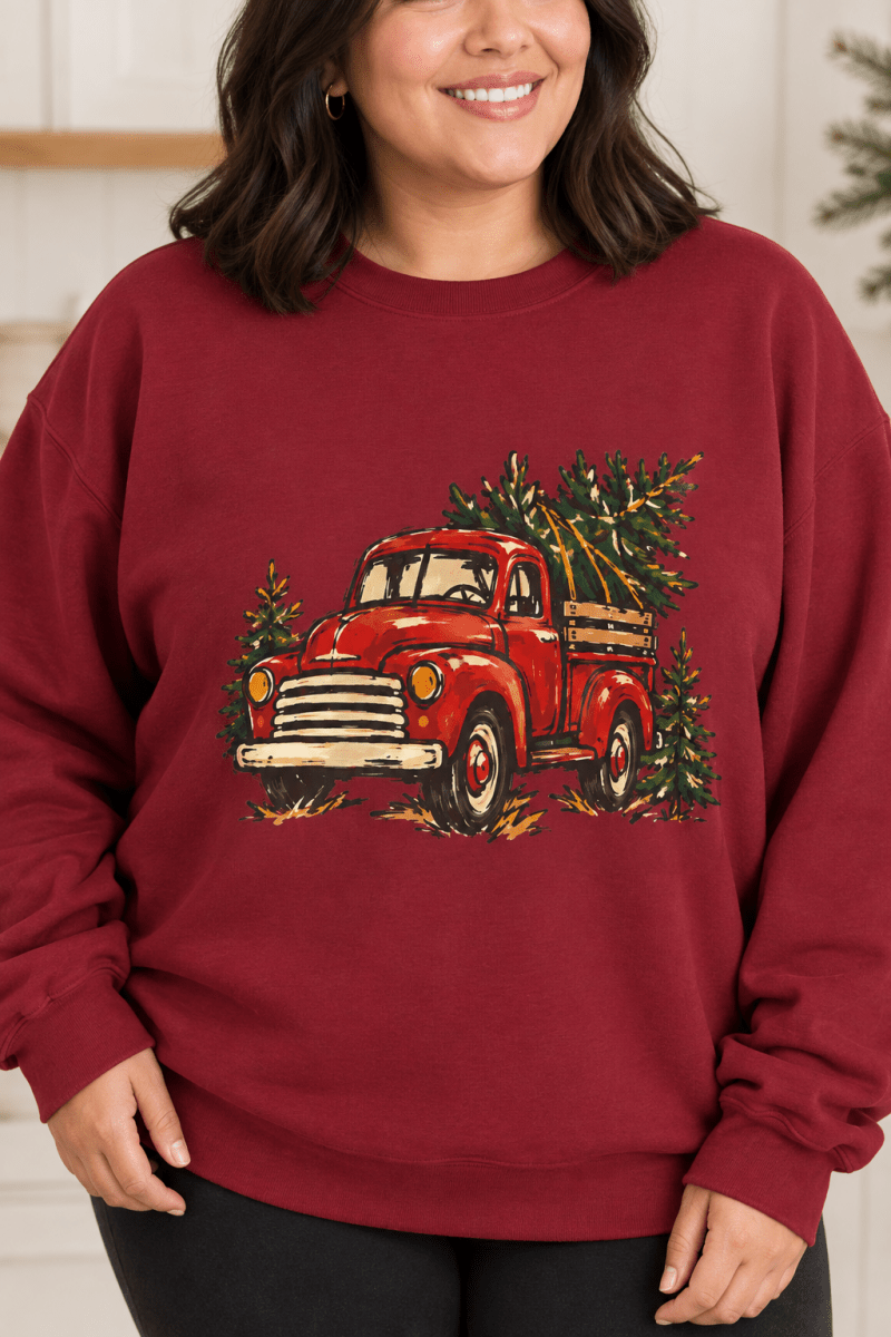 The Doodled Flower Boutique cardinal red crewneck sweatshirt featuring a textless vintage red Christmas truck carrying an evergreen tree graphic, close up.