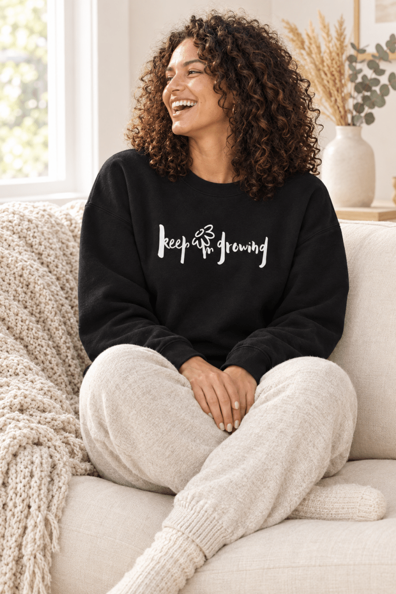 The Doodled Flower Boutique black keep growing crewneck sweatshirt styled with oatmeal knit joggers on a cozy cream sofa.