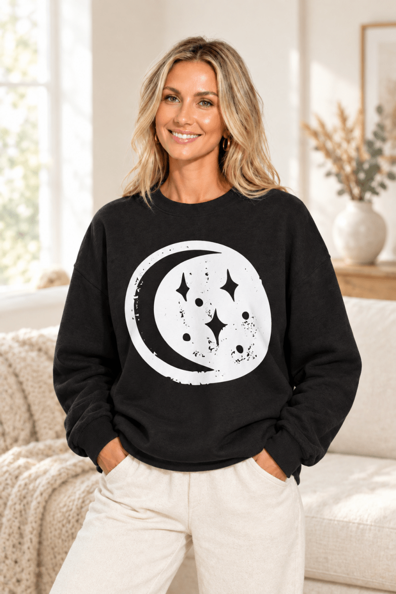 The Doodled Flower Boutique black crewneck sweatshirt featuring an original moon and stars graphic, close up.