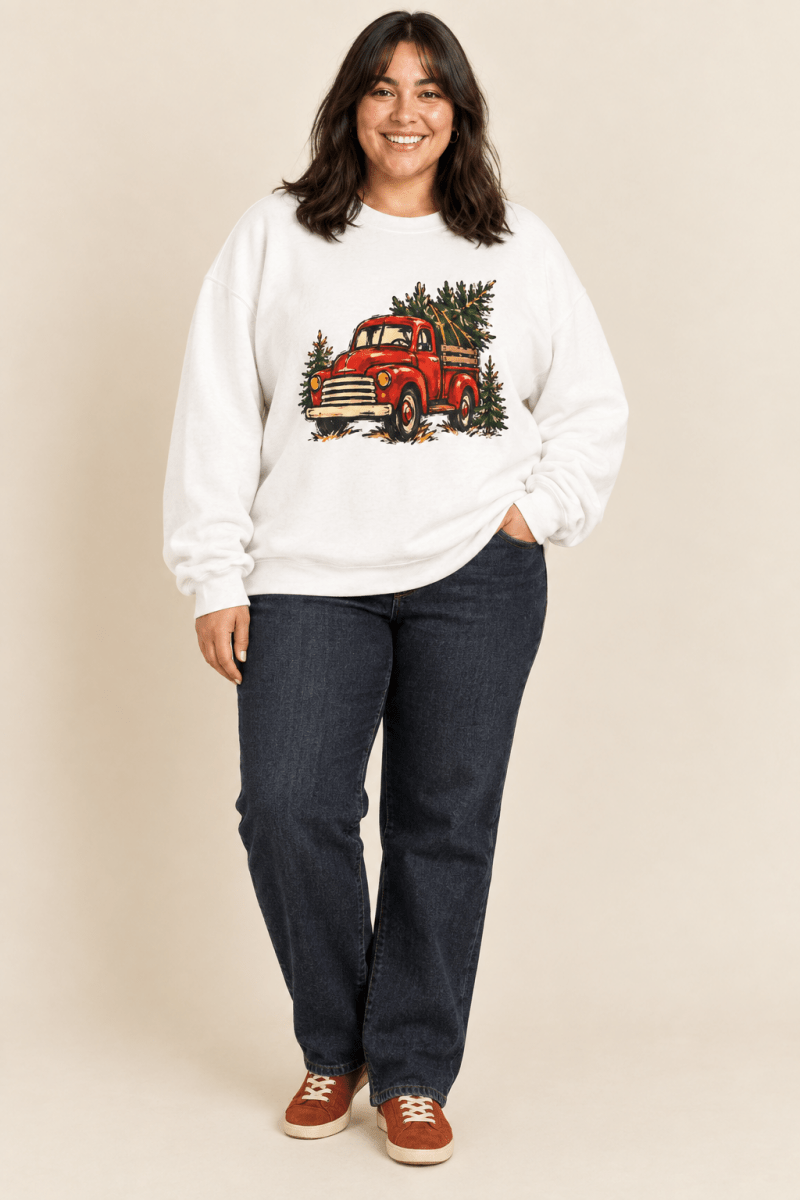 The Doodled Flower Boutique white crewneck sweatshirt featuring a textless vintage red Christmas truck carrying an evergreen tree graphic, worn by a model.