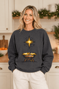 The Doodled Flower Boutique dark heather crewneck sweatshirt featuring a star of Bethlehem and manger graphic, close up in a Christmas kitchen.