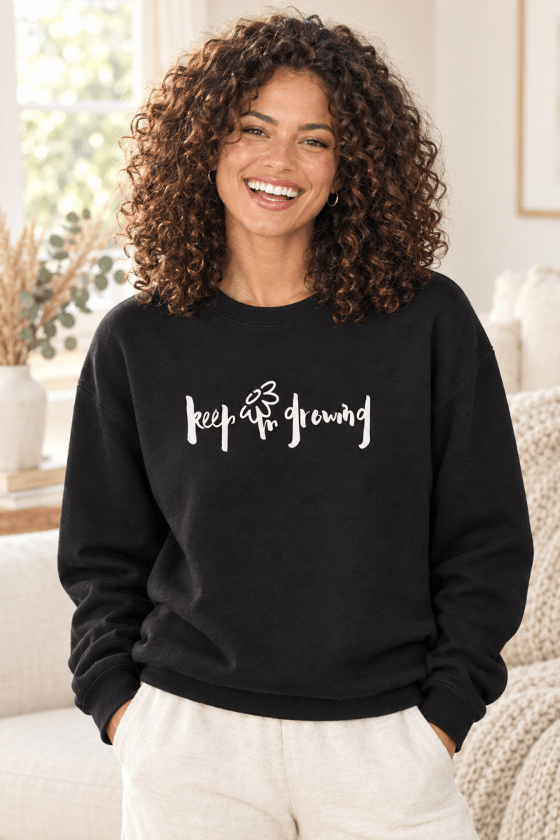 The Doodled Flower Boutique black crewneck sweatshirt featuring an original hand-lettered keep growing graphic with a doodled daisy, close up.