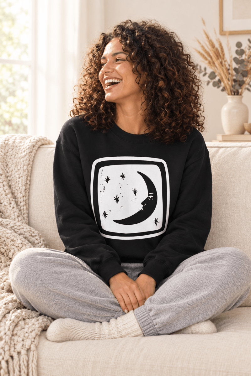 The Doodled Flower Boutique black crescent moon and stars crewneck sweatshirt styled with grey knit joggers on a cozy cream sofa.