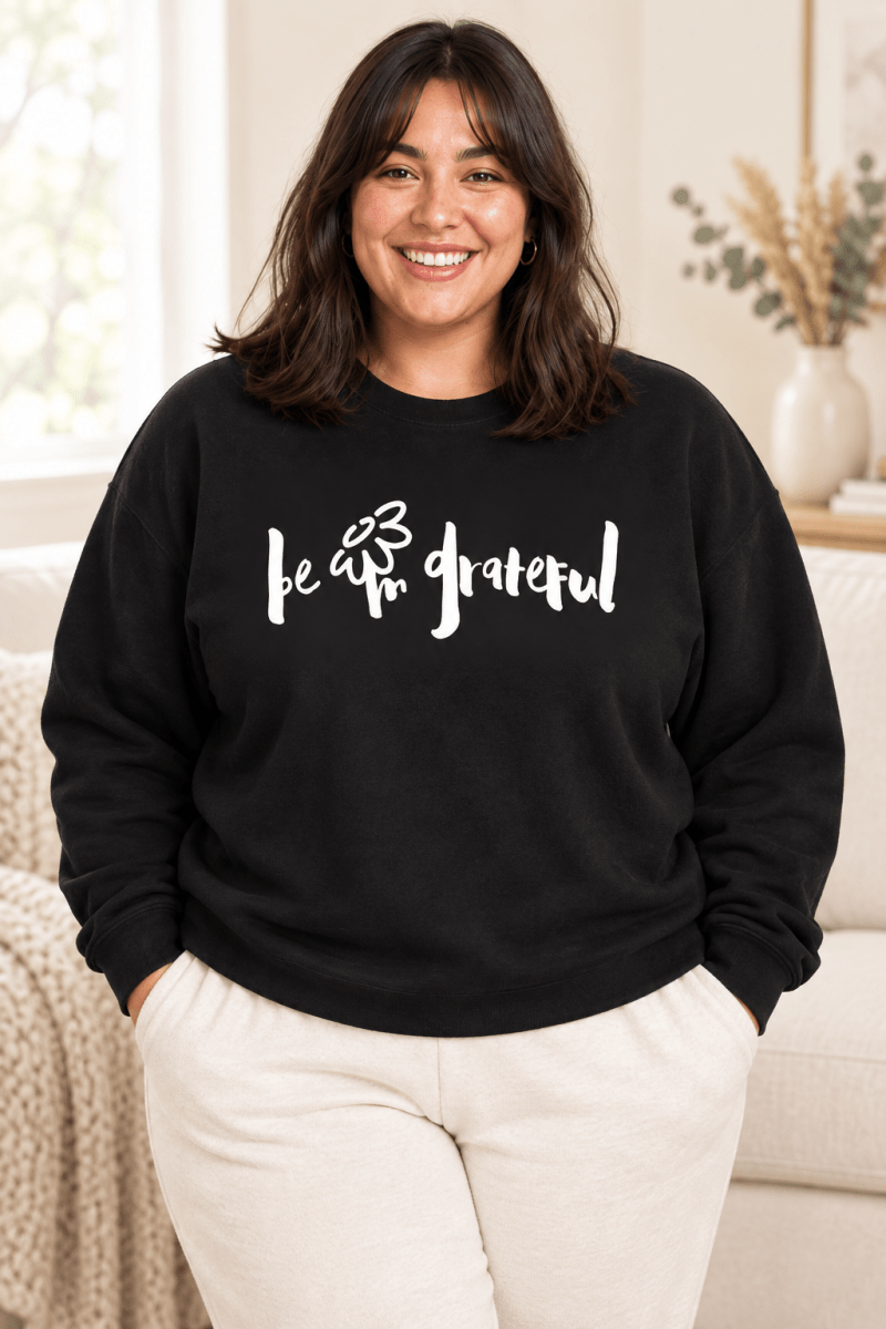 The Doodled Flower Boutique black crewneck sweatshirt featuring an original hand-lettered be grateful graphic with a doodled daisy, close up.