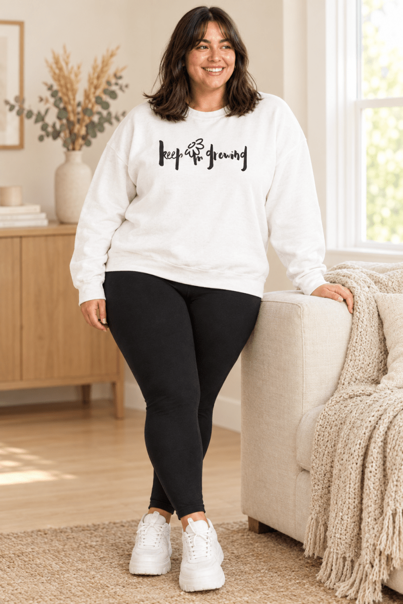 The Doodled Flower Boutique white keep growing crewneck sweatshirt styled with black leggings in a cream living room.