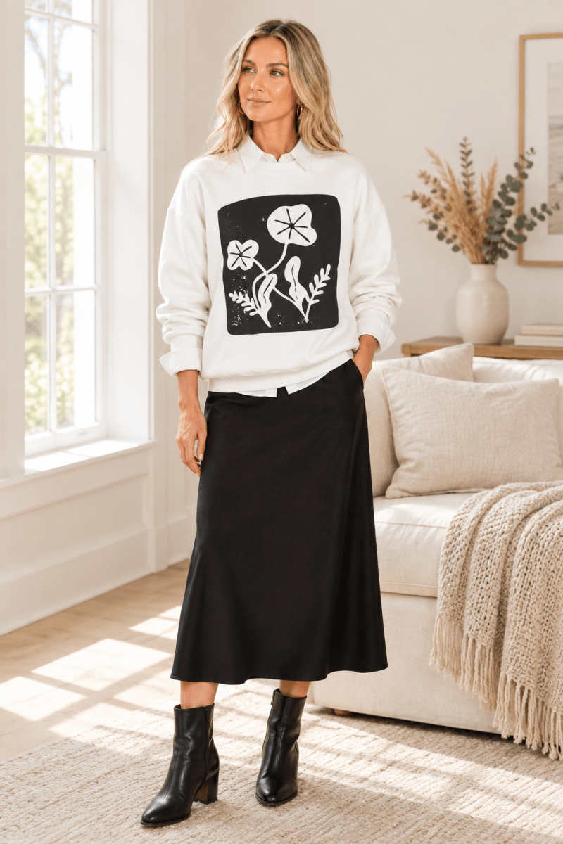 The Doodled Flower Boutique white floral block print crewneck sweatshirt layered over a white button-down with a black midi skirt and ankle boots.