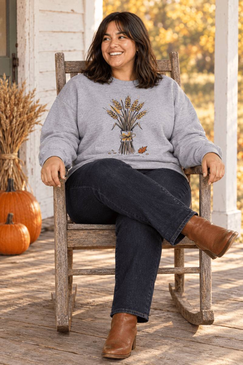 The Doodled Flower Boutique sport grey wheat bouquet crewneck sweatshirt styled with dark jeans and cognac ankle boots in a porch rocking chair.