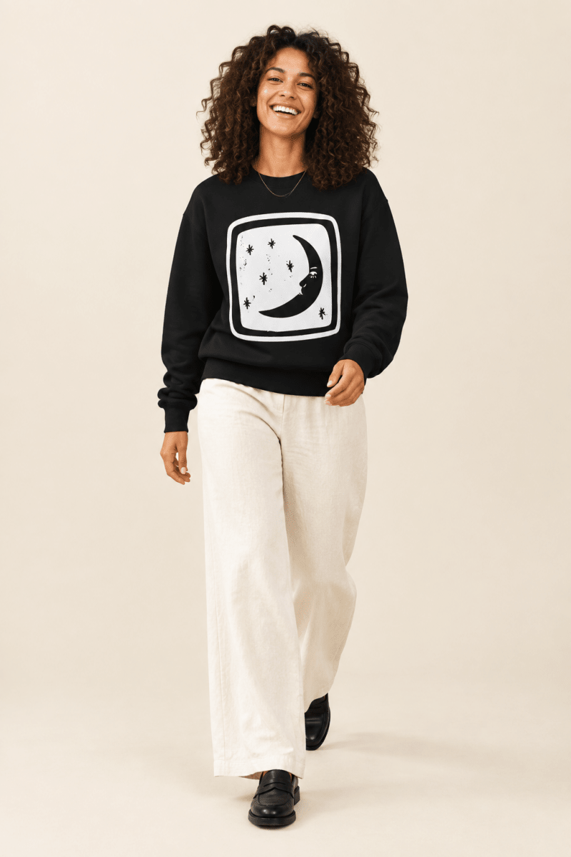 The Doodled Flower Boutique black crescent moon and stars crewneck sweatshirt worn by a model with ivory wide leg trousers and black loafers.